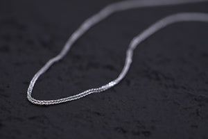 Close-up of a delicate silver chain on black. Intricate design, polished shine. Minimalist, elegant style.