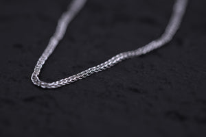 Close-up of a delicate silver chain shimmering on a black background. Intricate design showcases elegant craftsmanship. Tibetan prayer beads.