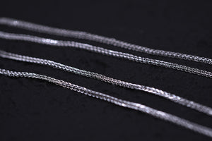 Four delicate silver chains shimmer against black, showcasing their intricate textured weave. Tibetan prayer beads bracelet inspiration.