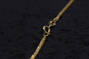 Close-up of a detailed gold necklace clasp on dark fabric. Reflective gold chain and clasp. Amulet necklace.