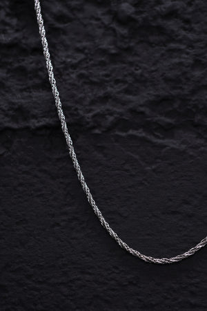 Close-up of a thin, twisted silver rope chain on a textured black background. Ideal for Tibetan dzi beads or other spiritual jewelry.