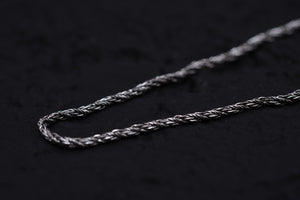 Close-up of antique silver braided chain on black background. Rustic Tibetan bracelet detail.