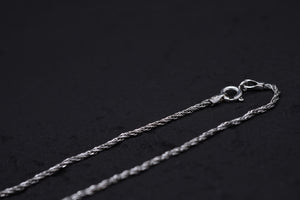 Sleek braided silver chain gleaming against a black backdrop. Close-up showcases texture and clasp. Ideal for amulet necklace.