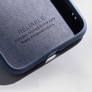 Close-up of a textured, slate blue phone case corner. Soft, matte finish with "Baby skin feeling" embossed. Minimalist product shot.