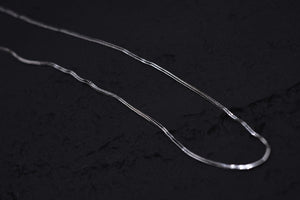 Close-up of a delicate, shimmering silver herringbone chain necklace on a black background. Minimalist, elegant jewelry for everyday wear.