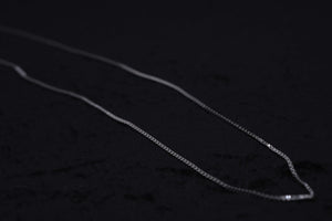 Delicate silver chain necklace close-up on dark textured background. Simple, elegant jewelry for everyday wear.