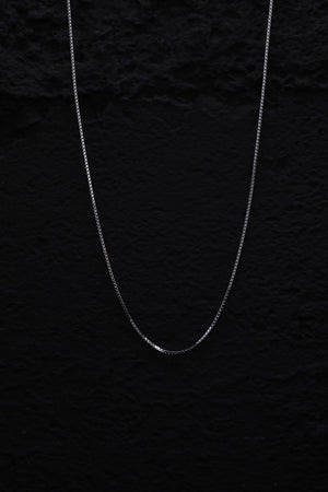 Close-up of a delicate silver box chain necklace shimmering against a black background. Classic, versatile design.