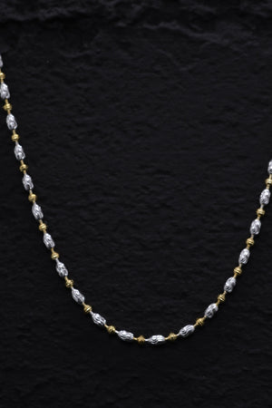Elegant two-tone necklace with alternating silver oblong links and gold beads on a textured black background.