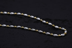 Close-up of a two-tone gold & silver chain necklace with delicate, textured oval links. Showcase of craftsmanship.
