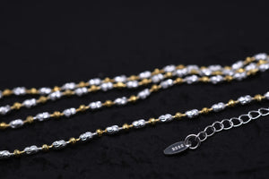 Close-up of a silver & gold Tibetan dzi bead necklace on black. S925 tag signifies sterling silver. Intricate, two-tone design.