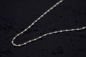 Close-up of a delicate gold & silver chain necklace on black. Intricate oval links highlight the two-tone design. Amulet necklace.