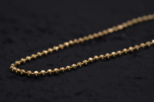 Close-up of a delicate gold beaded chain on black. Elegant, simple style. Tibetan dzi beads jewelry.