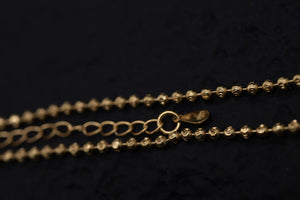 Elegant gold beaded chain necklace on dark background. Close-up showcases textured Tibetan dzi-style beads and clasp.