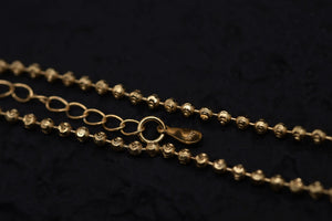 Close-up of gold beaded chain necklace on black fabric. Detailed product shot showcasing textured Tibetan dzi beads and clasp.