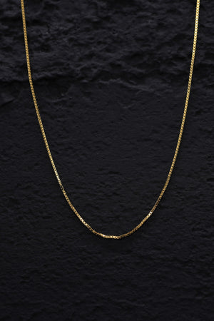 Close-up of a gleaming gold tone box chain necklace against a black background. Delicate craftsmanship shines. Sterling silver necklace.