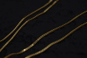 Shiny gold box chain necklace close-up on dark background. Elegant, simple design showcasing intricate detail. Amulet necklace for everyday wear.