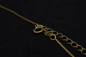 Close-up of elegant gold necklace clasp and extender chain on black background. Delicate amulet necklace with simple, classic style.