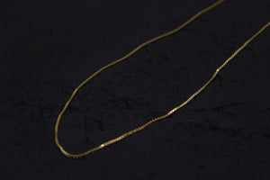 Elegant gold chain necklace on black background. Delicate, thin links create a simple, timeless design. Amulet necklace for everyday wear.