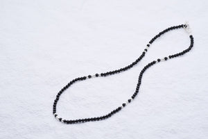 Delicate black beaded necklace with silver accents on a white background. Simple, minimalist Tibetan dzi bead jewelry.