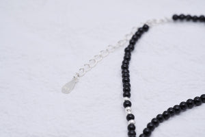 Elegant black beaded bracelet with silver accents on a textured white background. Minimalist style with tiny silver spacer beads and delicate chain extender. Buddhist prayer beads for meditation.