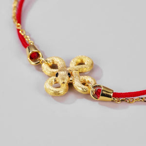 Gold snake charm bracelet on red cord. Intricate knotted design with textured detail. Buddhist prayer beads for elegant, simple style.