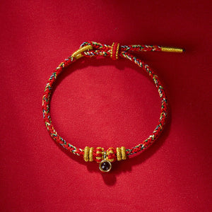 Braided cord bracelet in red, white, green & blue with gold accents, sliding knot & purple gemstone charm on red..