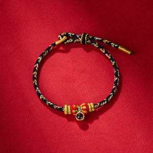Braided bracelet with red, green, and gold threads, textured gold and red beads, and gemstone accent.