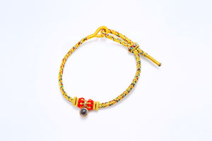 Gold braided bracelet with adjustable knot, red beads, and dark gray pendant.