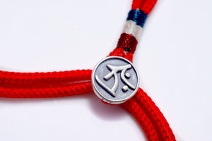 Red braided bracelet with silver "K" charm and blue, white accents. Tibetan dzi beads style.