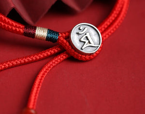 Red braided bracelet with silver "Hung" charm and teal accents. Tibetan Dzi bead style.