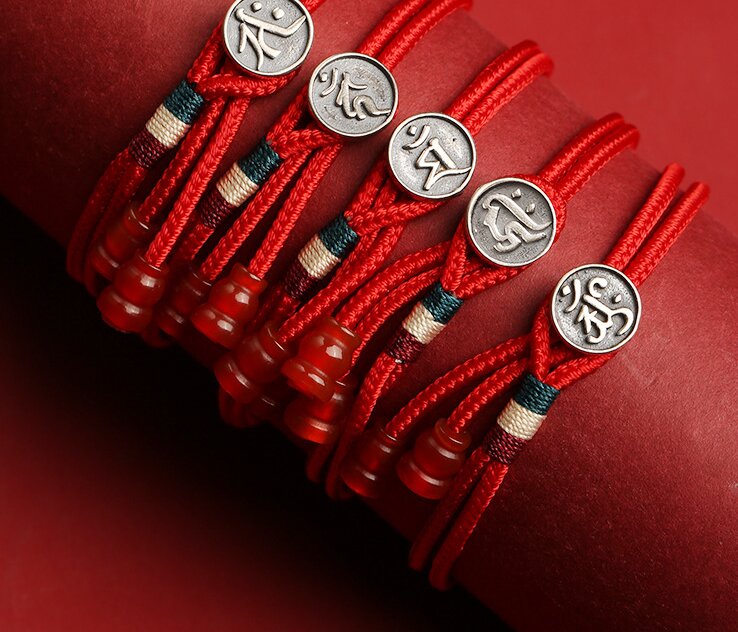 Red string bracelets with silver Tibetan dzi beads on a red background. Spiritual protection and blessings for balance and harmony.
