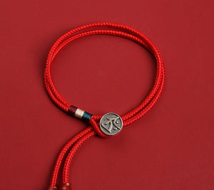Close-up of red braided cord bracelet with silver charm and dzi beads on red background. Minimalist Tibetan style.