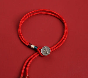 Red braided cord bracelet with Om charm and Tibetan dzi-style beads on a red background. Simple, minimalist style.