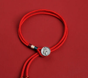 Close-up of red braided dzi beads bracelet on matching background. Silver charm, wood accents, minimalist style. Tibetan prayer beads for mindful meditation.
