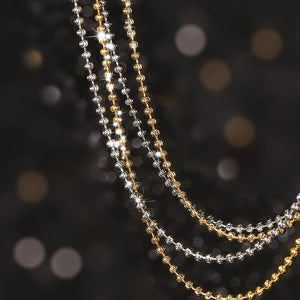 Close-up of shimmering gold & silver beaded necklaces on a dark background. Elegant moon-cut design showcases craftsmanship. Tibetan dzi beads?