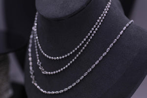 Close-up of three silver necklaces with beaded and textured oval links on a dark bust. Showcase of Tibetan dzi beads jewelry.