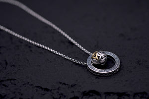 Elegant silver necklace with intricate circular dzi bead pendant, partially gold, on a delicate chain. Tibetan dzi beads jewelry.