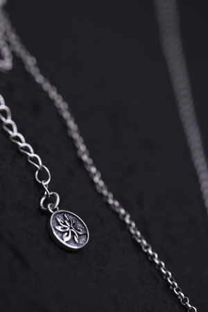 Close-up of a silver floral pendant necklace on a dark background. Tibetan dzi beads inspire this delicate, stylish piece.