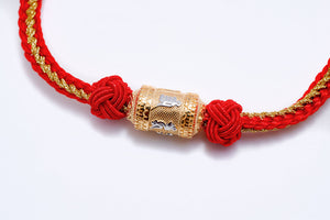 Close-up of a red and gold Tibetan dzi bead bracelet. The gold bead with embossed symbols is nestled between knotted cord, creating a clean, stylish look.