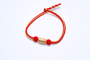 Red and gold woven Tibetan bracelet with gold charm, knotted for a simple, elegant style.