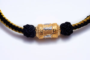 Close-up of a stylish black and gold braided bracelet featuring a Tibetan Dzi bead with etched silver details.