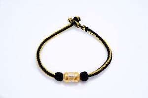 Gold Tibetan dzi bead bracelet on white background. Etched cylindrical bead with black and gold braided cord. Simple, stylish.