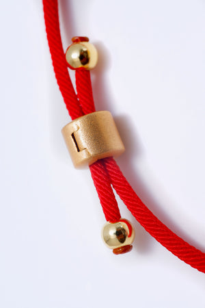 Elegant red cord bracelet with gold cylindrical dzi bead and accents. Simple Tibetan style.