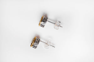 Close-up of ornate Tibetan dzi bead stud earrings. Silver patterned bands frame gold centers. Simple, elegant style.