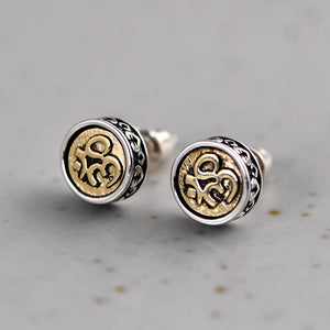 Close-up of Tibetan amulet earrings: silver etched rings with gold Om symbols. Protection and abundance.