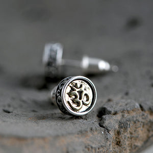 Close-up of silver Om stud earrings on a textured stone. Tibetan Buddhist inspired design with detailed craftsmanship.