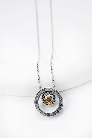Elegant silver necklace with circular pendant featuring an ornate gold dzi bead. The eye motif and white stone add a mystical touch.