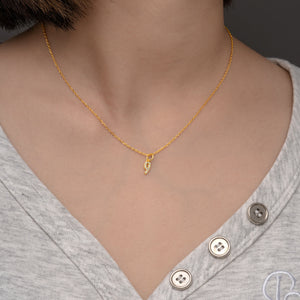 Gold necklace with diamond "9" pendant on person wearing grey v-neck.