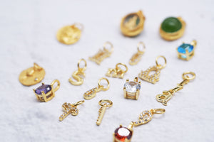 Gold letter, gemstone, & religious charms scattered on white. Includes cross, key, & alphabet.