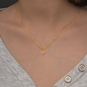 Gold necklace with small pendant charm on person in grey t-shirt. Delicate initial necklace.